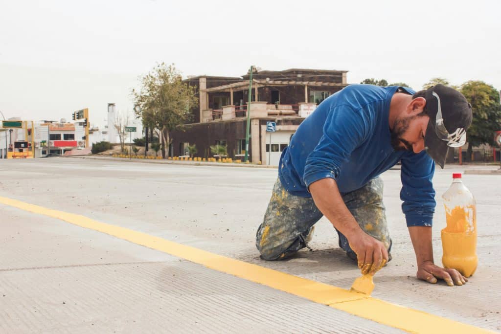 A man paints yellow road lines on an urban street, emphasizing urban infrastructure and maintenance.