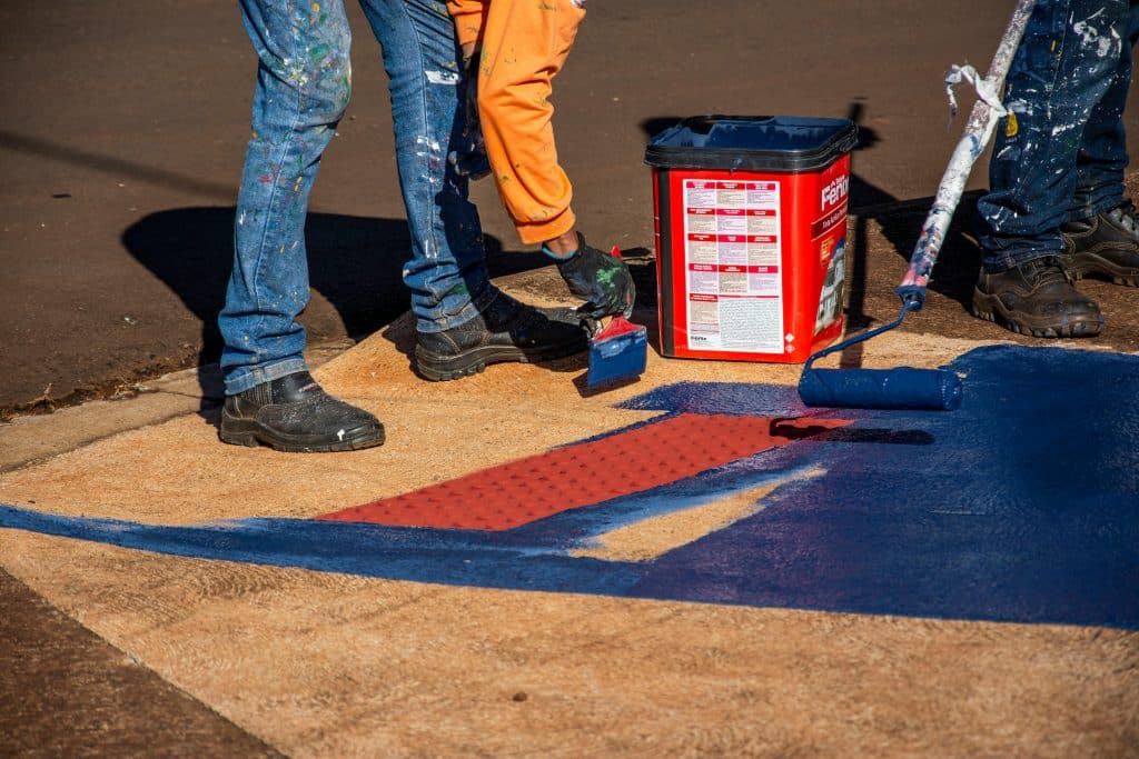Close-up of workers painting a pavement with blue and red paint using rollers in Londrina, Brazil.